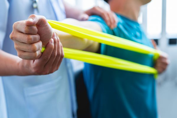 Physical therapist gives resistance band exercises. About the arms and shoulders of male office workers, office syndrome, male patient. Physiotherapy concept.